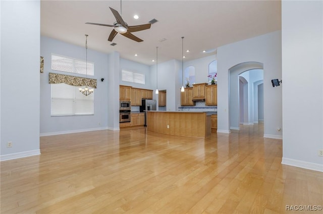 kitchen with brown cabinetry, appliances with stainless steel finishes, a center island, light wood-type flooring, and pendant lighting