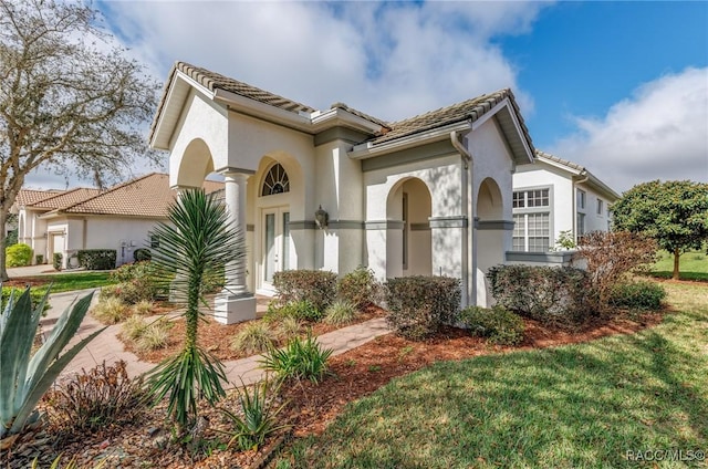 mediterranean / spanish-style home featuring a front yard, a tiled roof, and stucco siding