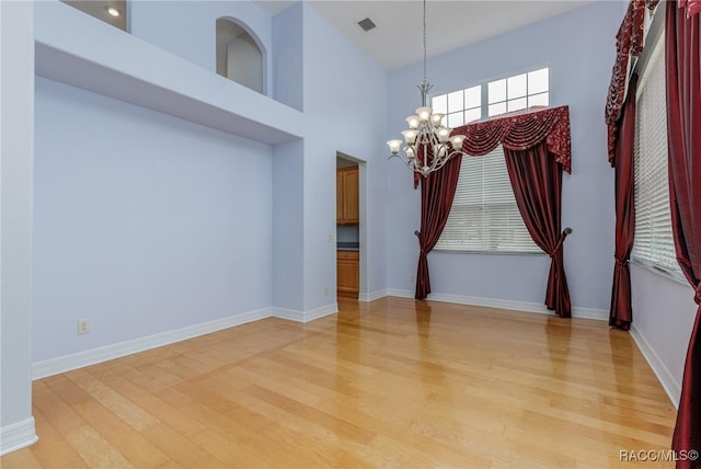 unfurnished dining area featuring baseboards, a high ceiling, light wood-style flooring, and an inviting chandelier