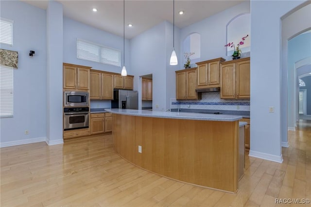 kitchen with a center island with sink, appliances with stainless steel finishes, pendant lighting, and light countertops