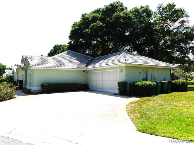 view of home's exterior with driveway, a tiled roof, an attached garage, a yard, and stucco siding
