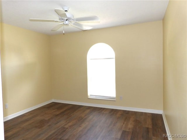 unfurnished room featuring a ceiling fan, baseboards, and dark wood finished floors