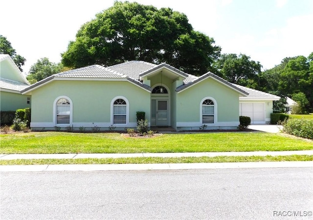 single story home with an attached garage, a tile roof, a front yard, and stucco siding