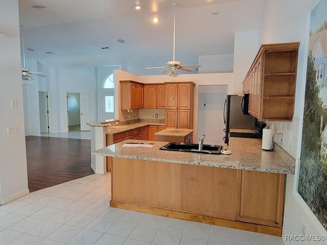 kitchen with light hardwood / wood-style floors, light stone countertops, kitchen peninsula, and sink