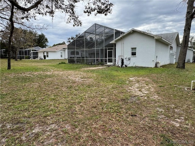 rear view of house with a lawn, glass enclosure, and stucco siding