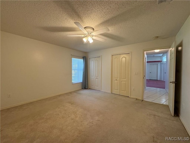 unfurnished bedroom featuring light colored carpet, a textured ceiling, multiple closets, and baseboards