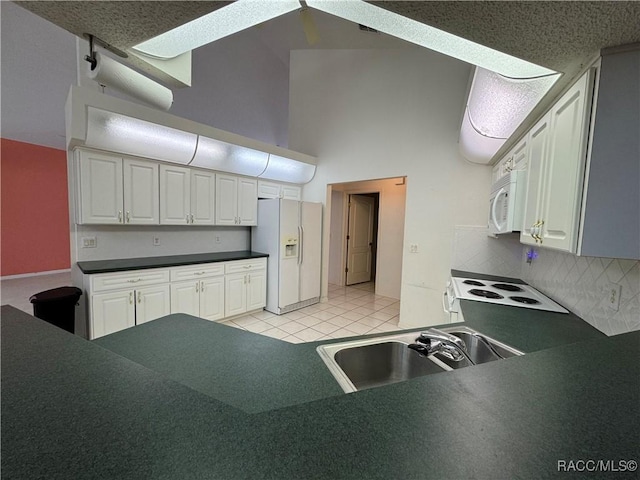 kitchen featuring dark countertops, white cabinets, white appliances, and a high ceiling