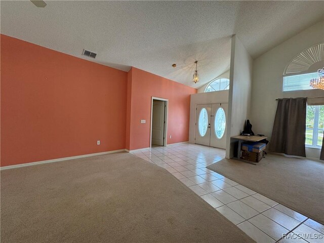 foyer entrance featuring light tile patterned flooring, light colored carpet, a textured ceiling, baseboards, and visible vents