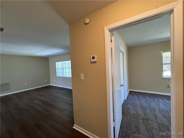 corridor featuring visible vents, a textured ceiling, and baseboards