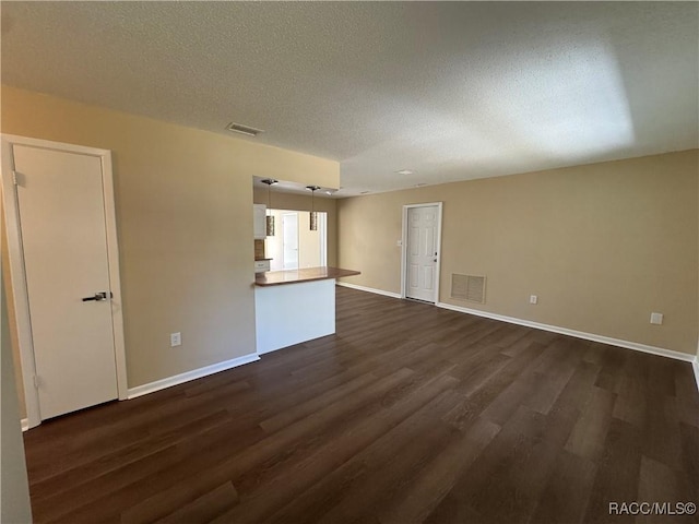 spare room featuring dark wood finished floors, visible vents, a textured ceiling, and baseboards