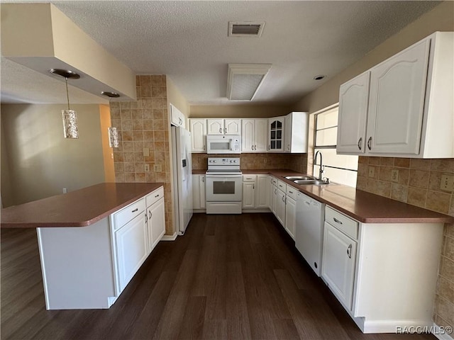 kitchen with visible vents, dark wood-type flooring, a sink, white appliances, and a peninsula