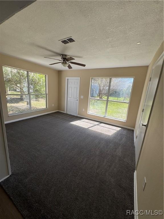 empty room with visible vents, baseboards, a ceiling fan, and dark carpet