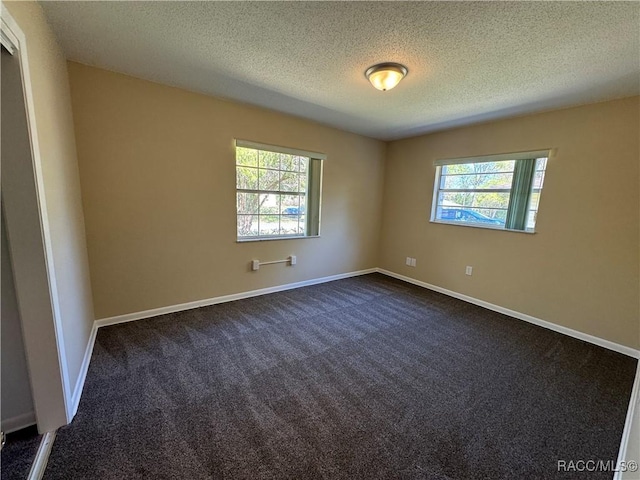 empty room with plenty of natural light, dark carpet, and baseboards