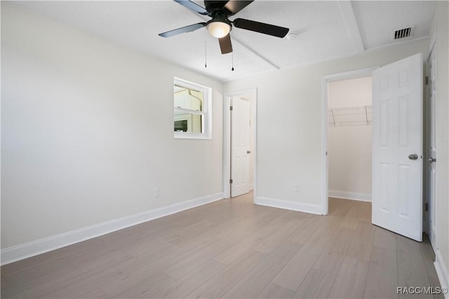 unfurnished bedroom with visible vents, a closet, light wood-style floors, baseboards, and a walk in closet