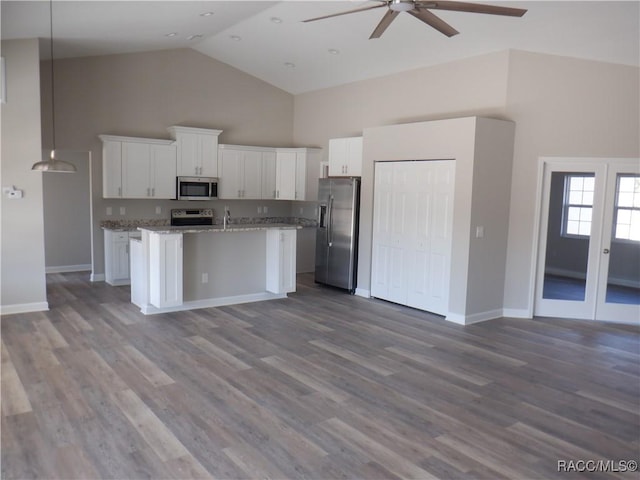 kitchen with stainless steel appliances, light stone counters, an island with sink, white cabinets, and decorative light fixtures