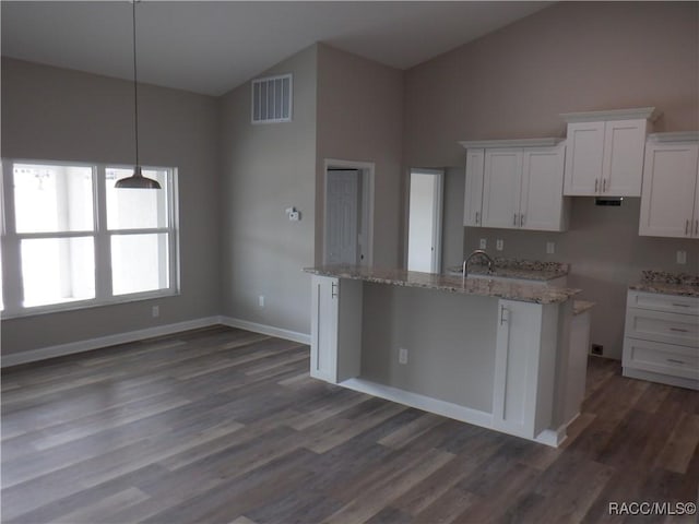 kitchen featuring pendant lighting, dark wood-type flooring, light stone countertops, white cabinets, and a center island with sink