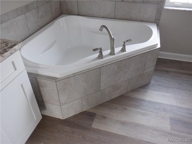 bathroom with a relaxing tiled tub, vanity, and hardwood / wood-style flooring