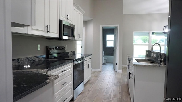 kitchen featuring appliances with stainless steel finishes, sink, light hardwood / wood-style flooring, dark stone countertops, and white cabinetry