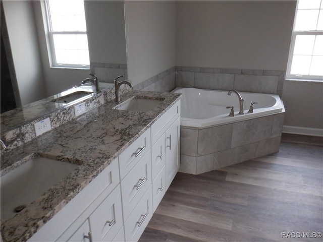 bathroom with a healthy amount of sunlight, tiled bath, and vanity