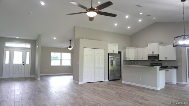 kitchen featuring high vaulted ceiling, white cabinets, appliances with stainless steel finishes, decorative light fixtures, and light hardwood / wood-style floors