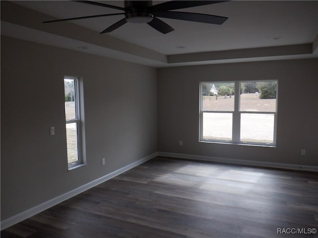 empty room with dark wood-type flooring, a raised ceiling, and ceiling fan