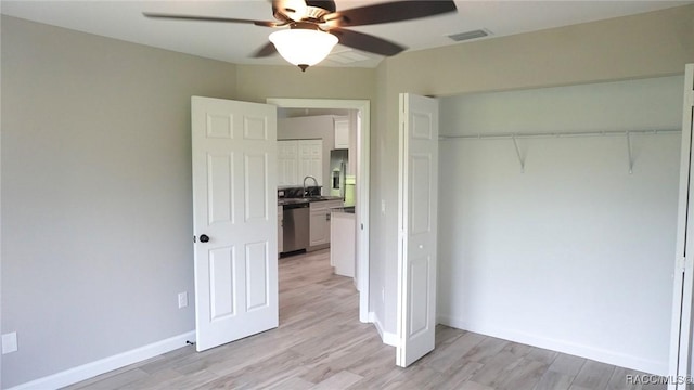 unfurnished bedroom featuring stainless steel fridge, ceiling fan, sink, light hardwood / wood-style flooring, and a closet