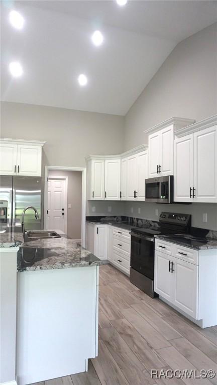 kitchen featuring white cabinets, stainless steel appliances, dark stone countertops, and sink