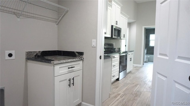 kitchen featuring appliances with stainless steel finishes, light hardwood / wood-style floors, white cabinetry, and dark stone countertops