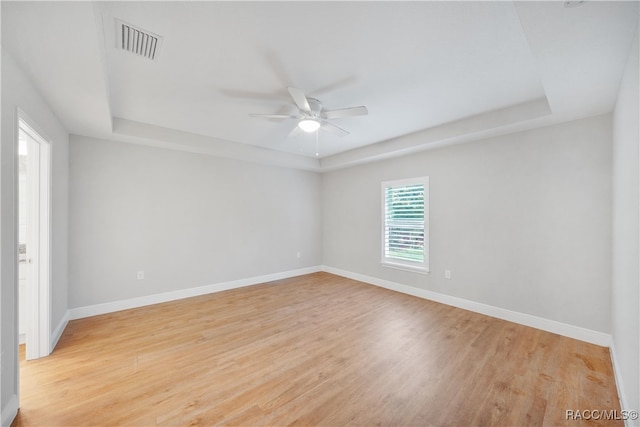 unfurnished room with ceiling fan, light hardwood / wood-style floors, and a raised ceiling