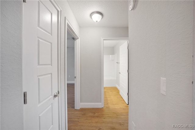 hall with a textured ceiling and light wood-type flooring