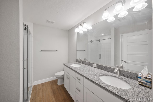 bathroom featuring vanity, wood-type flooring, toilet, a textured ceiling, and a shower with shower door