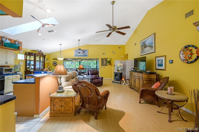 living room with a skylight, ceiling fan, high vaulted ceiling, and light wood-type flooring