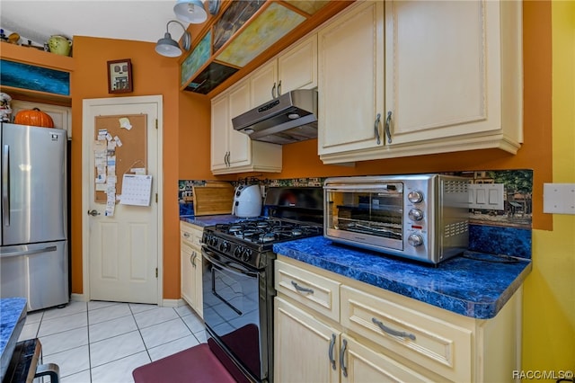 kitchen featuring stainless steel refrigerator, black gas stove, vaulted ceiling, cream cabinetry, and light tile patterned floors