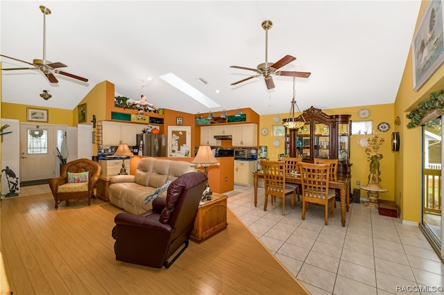 living room with high vaulted ceiling, a skylight, light hardwood / wood-style flooring, and ceiling fan