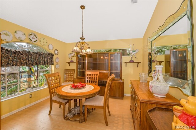 dining room with a notable chandelier, light hardwood / wood-style floors, and vaulted ceiling