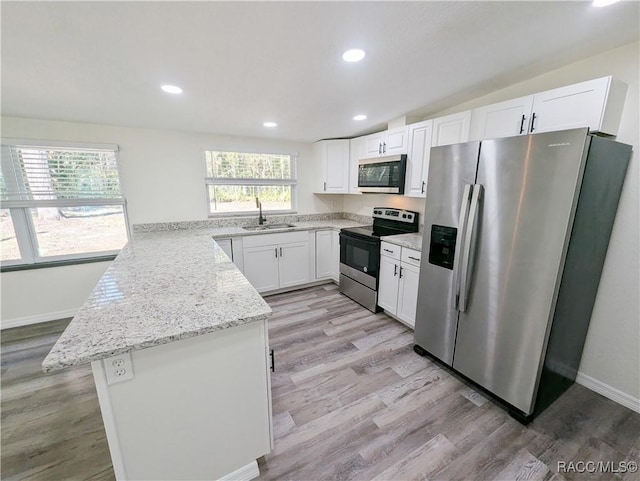 kitchen with appliances with stainless steel finishes, white cabinets, light stone counters, and light hardwood / wood-style flooring