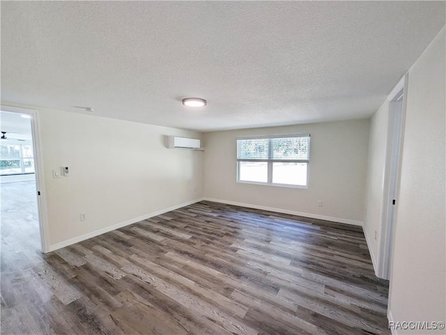 spare room featuring a wall mounted air conditioner, dark hardwood / wood-style floors, and a textured ceiling