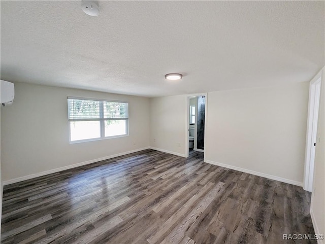 spare room with a wall unit AC, dark hardwood / wood-style flooring, and a textured ceiling