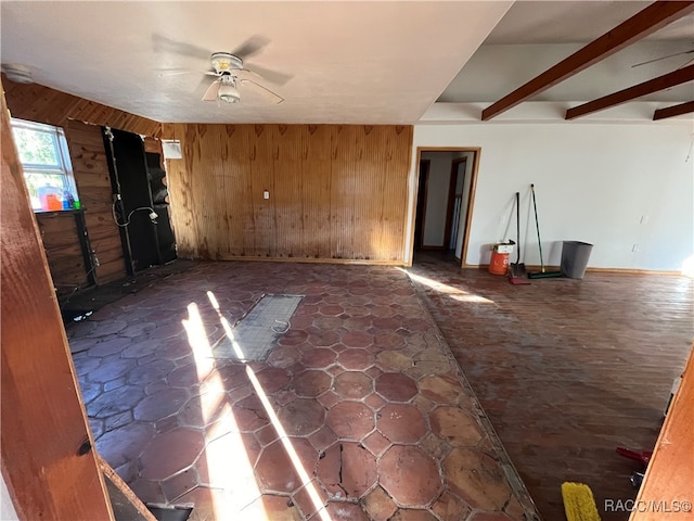 unfurnished room with beam ceiling, ceiling fan, and wood walls