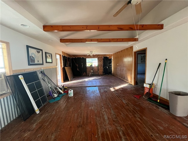 unfurnished living room with ceiling fan, wood walls, dark hardwood / wood-style flooring, and beam ceiling