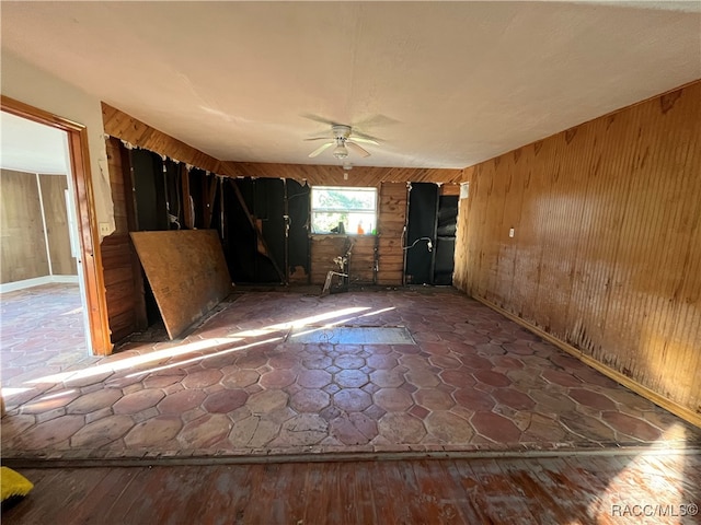 spare room featuring ceiling fan, wood-type flooring, and wood walls