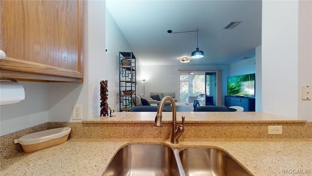 kitchen featuring light stone counters, decorative light fixtures, sink, and light brown cabinets