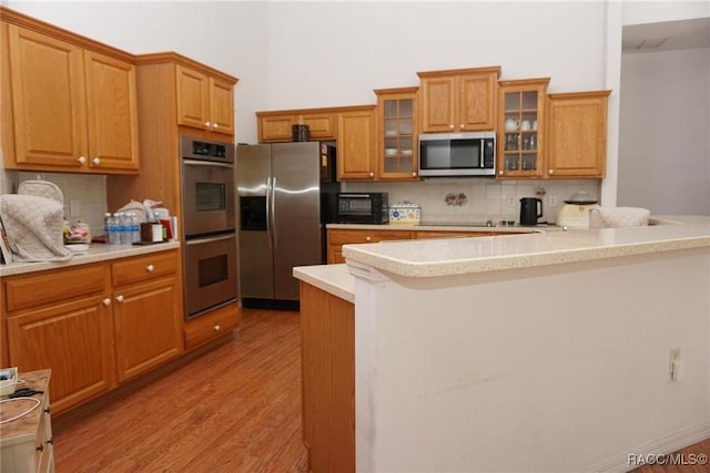 kitchen featuring light countertops, light wood-type flooring, tasteful backsplash, and black appliances