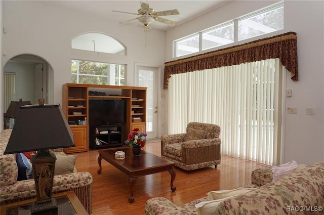 living area with a towering ceiling, a ceiling fan, plenty of natural light, and wood finished floors