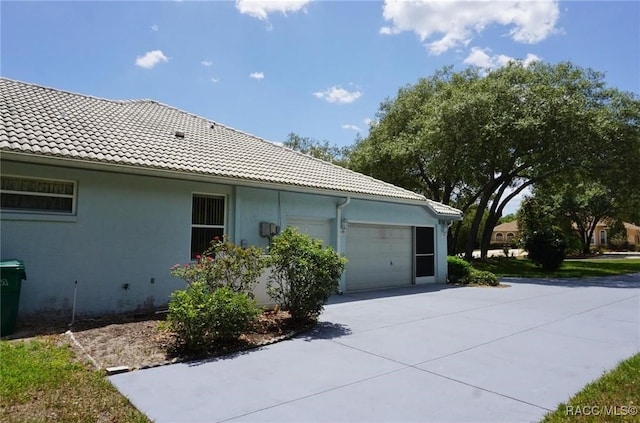 view of side of home featuring a tile roof, concrete driveway, a garage, and stucco siding