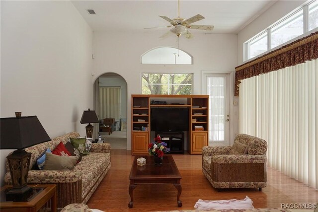living area with a ceiling fan, visible vents, wood finished floors, arched walkways, and a high ceiling