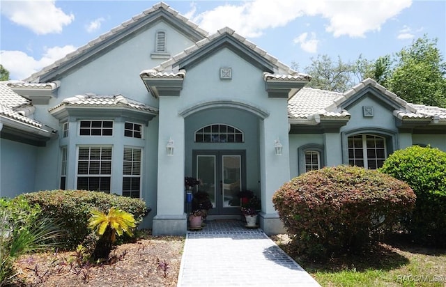 view of exterior entry featuring stucco siding, french doors, and a tile roof