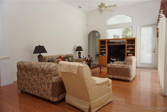 living area with wood finished floors, a high ceiling, visible vents, ceiling fan, and arched walkways
