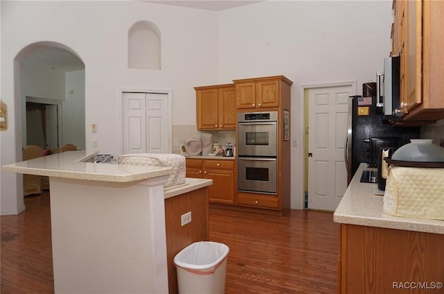 kitchen with stainless steel double oven, light countertops, dark wood-type flooring, and arched walkways