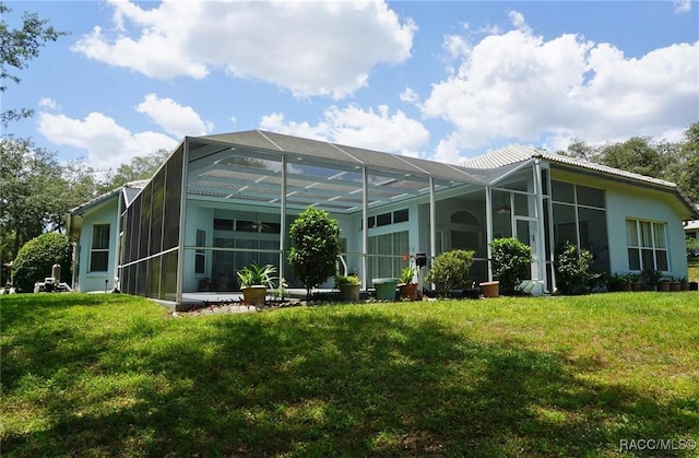 back of house featuring stucco siding, glass enclosure, and a lawn